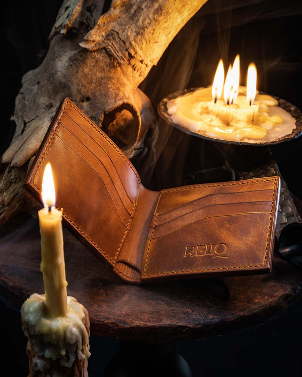 Open leather bifold wallet revealing a smooth brown interior with hand-stitched card slots, resting on a wooden surface next to a lit candle.