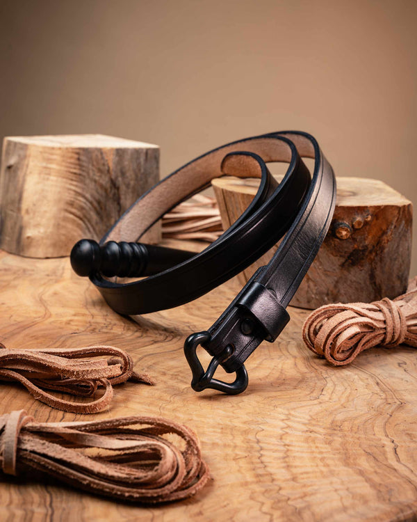 Handcrafted black leather medieval belt coiled on a wooden surface, featuring a historical replica buckle and creased edge detailing.