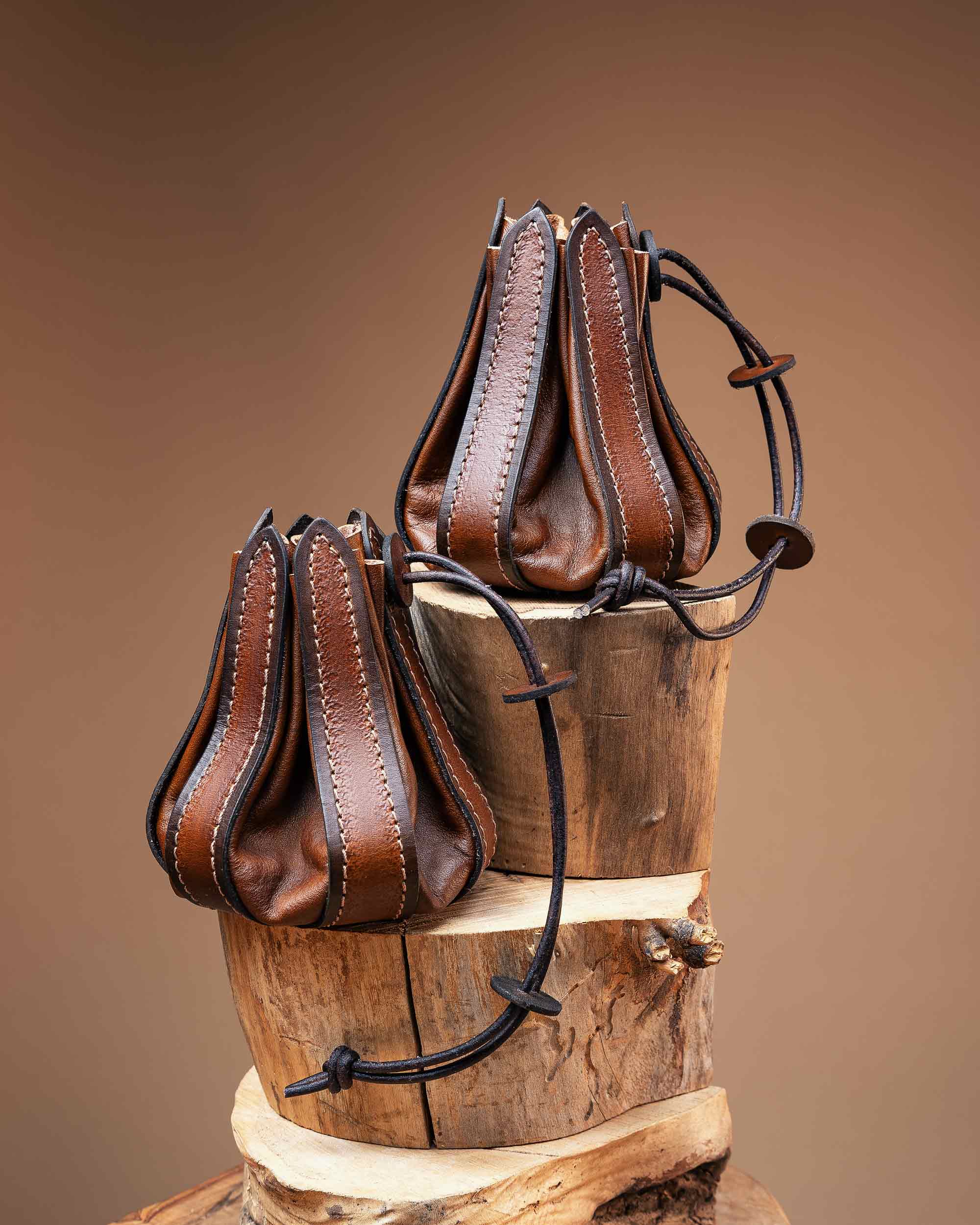 Two handcrafted brown leather drawstring pouches featuring a stitched bellows design, ideal for carrying RPG dice or everyday carry items.