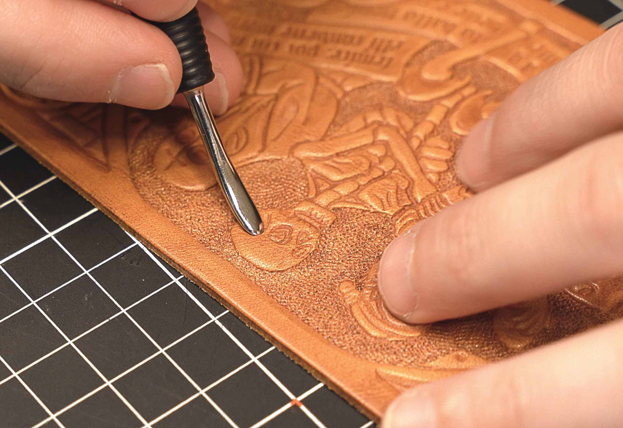 Close-up of Michele Belvedere working on a Danse Macabre-themed leather tooling for Reliq. The medieval skeleton figure is carved by hand on vegetable-tanned leather using traditional tools.