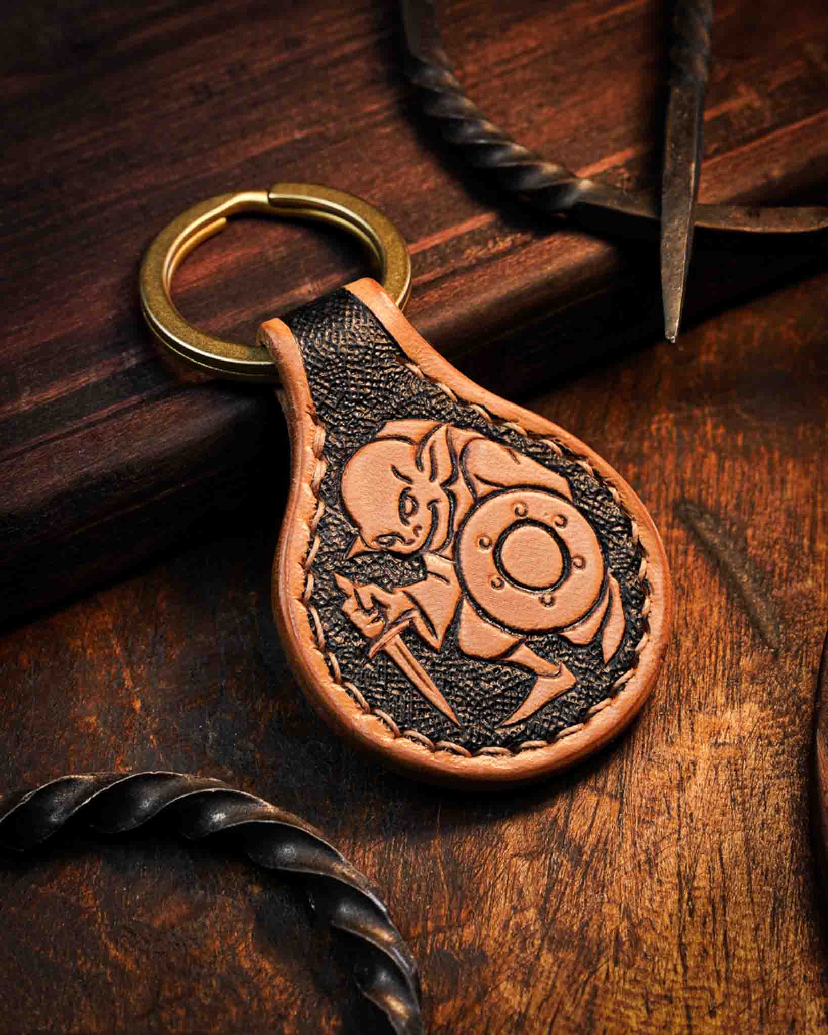 Handcrafted leather keychain featuring a hand-tooled goblin warrior holding a sword and shield, designed as a tabletop RPG accessory, set against a textured dark background with a solid brass ring.