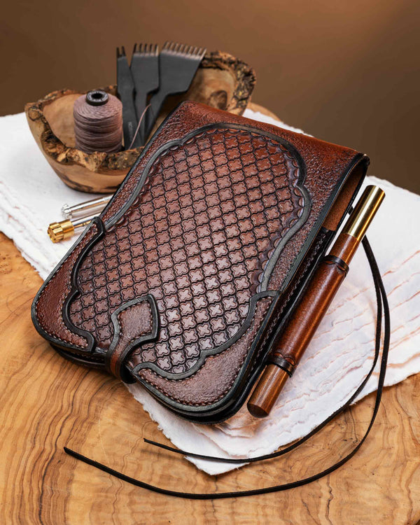 Closed brown leather A6 journal cover featuring an intricate hand-tooled geometric pattern, dark burnished edges, and a secure strap closure.