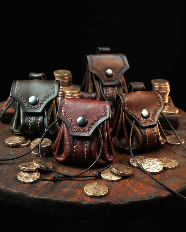 Collection of four handcrafted leather belt pouches in green, red, brown, and dark brown, featuring hand-tooled flaps and snap closures, surrounded by brass coins.