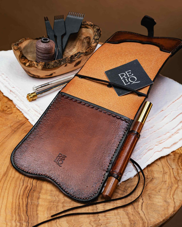 Interior view of an artisan leather notebook cover showing the smooth inner hide, an kangaroo leather holding lace, and the Reliq brand logo stamped on the lower pocket.