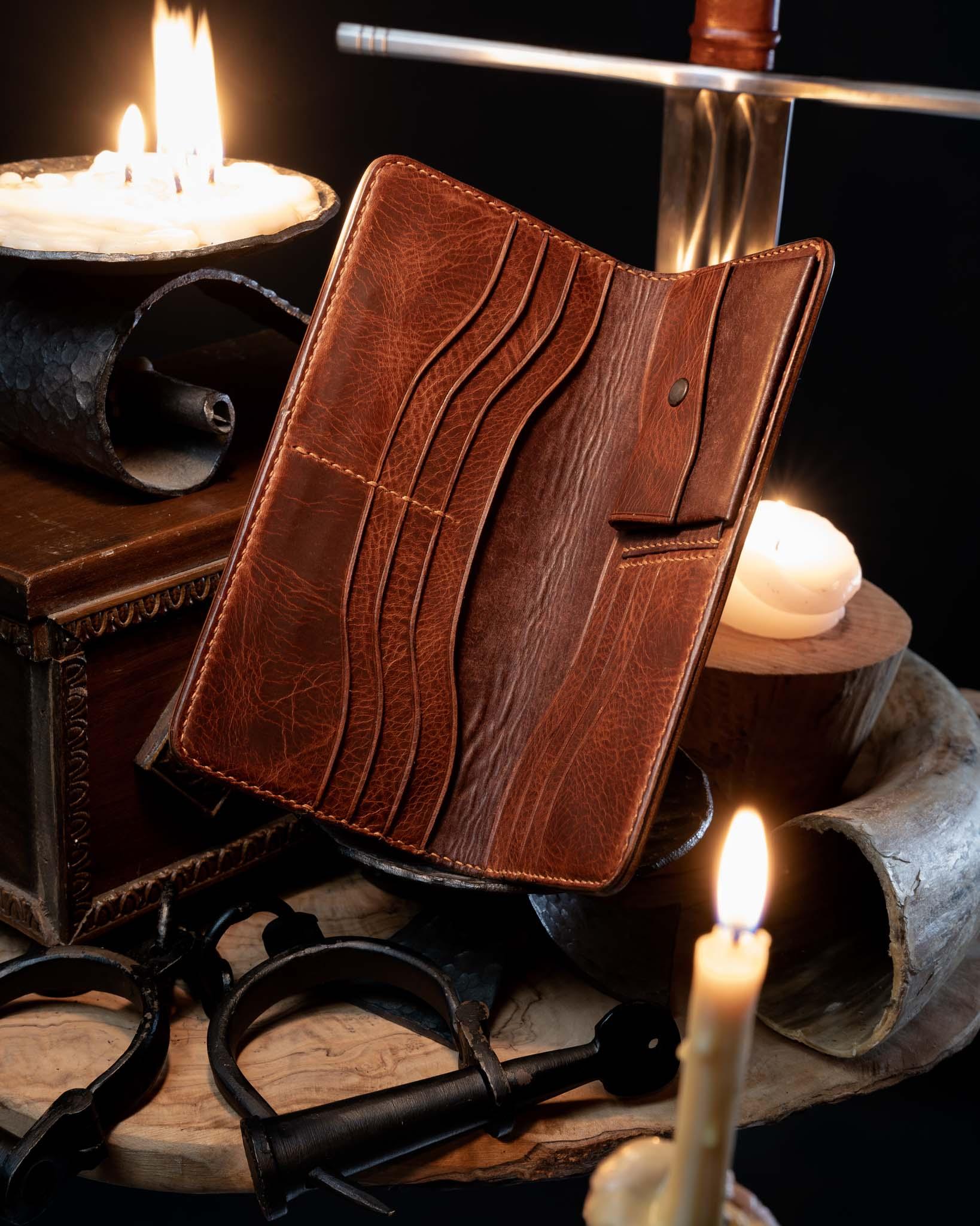 Open medieval leather long wallet revealing a spacious interior with multiple hand-stitched card slots and compartments, resting in a rustic candlelit setting.