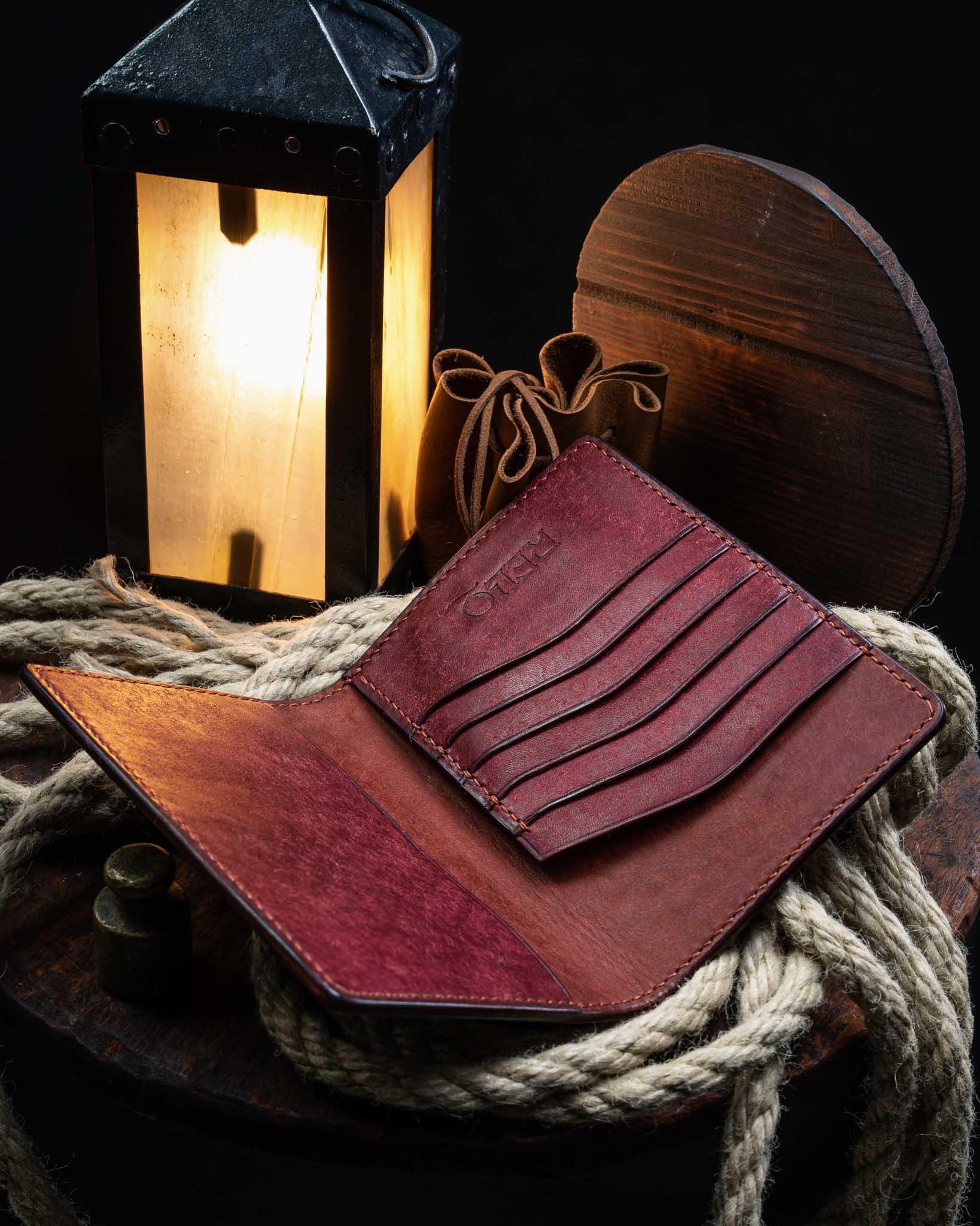 Angled view of the open handmade leather passport wallet, revealing securely stitched card slots and a rich reddish-brown interior finish next to a vintage lantern.