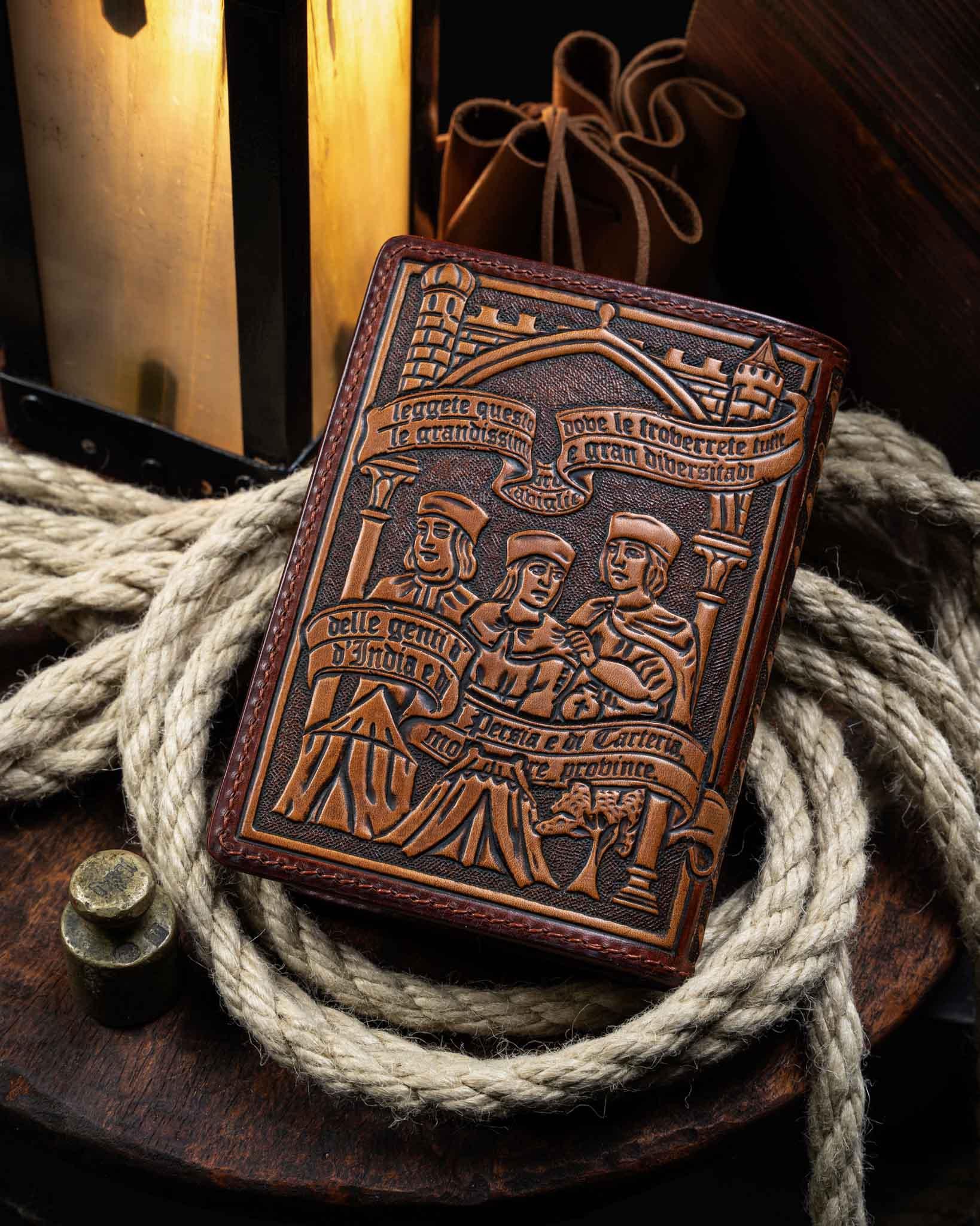 Back view of the hand-tooled leather passport wallet, displaying an intricate historical travel scene with figures and a tent carved into premium brown leather.