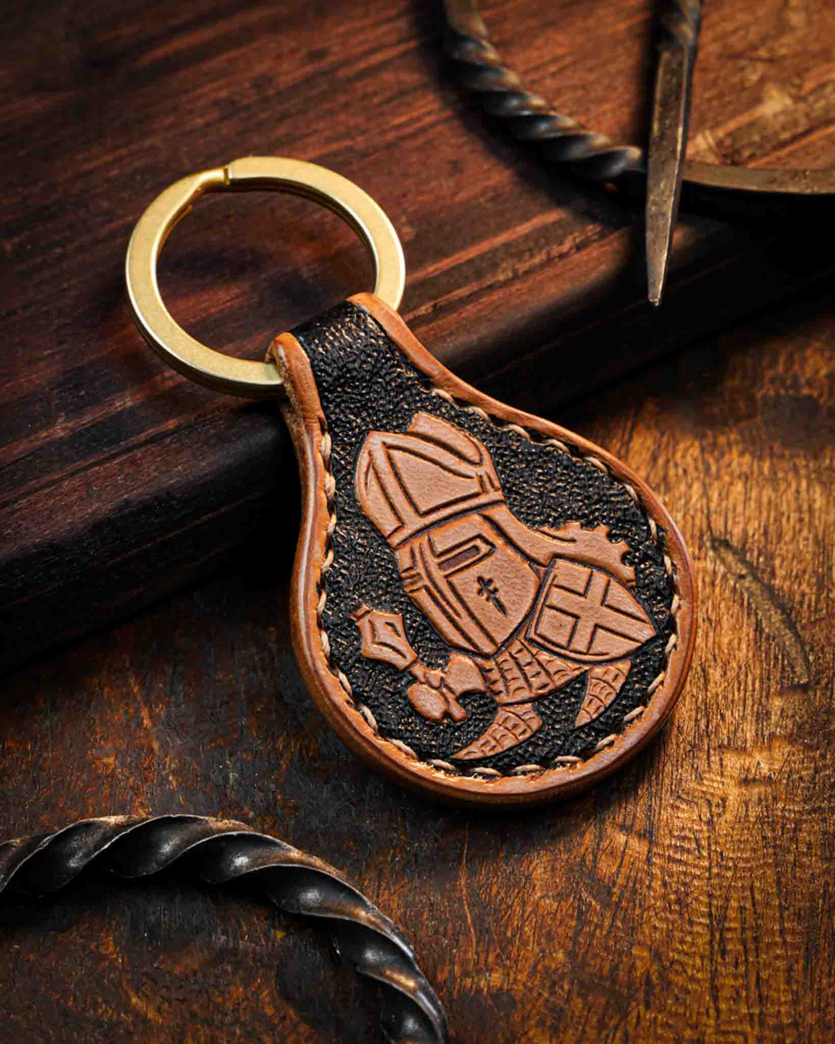Handcrafted leather keyring showcasing a hand-tooled medieval crusader mascot with a sword and shield, set against a textured dark background with a solid brass ring.