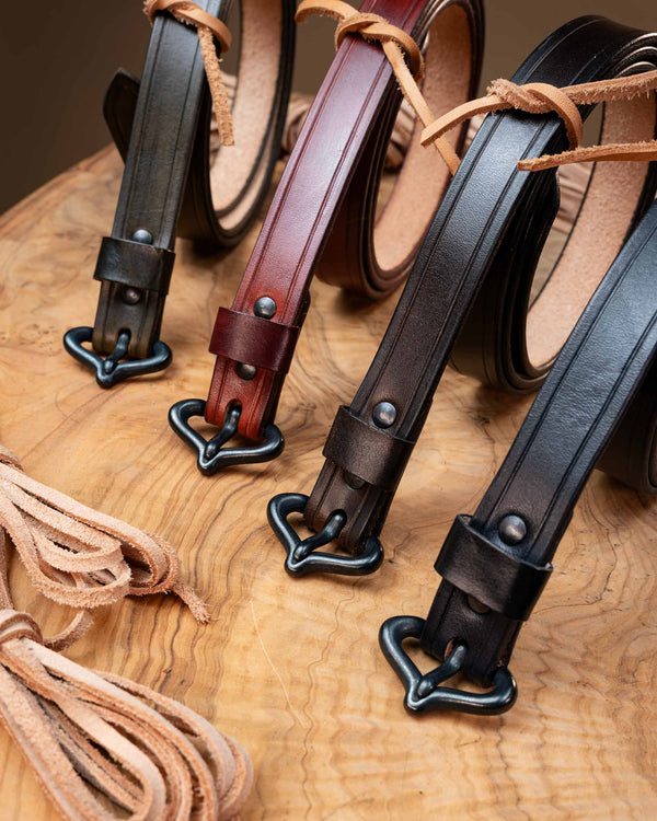 Collection of four handcrafted medieval leather belts in olive green, rustic red, dark brown, and black, all equipped with historical replica buckles.