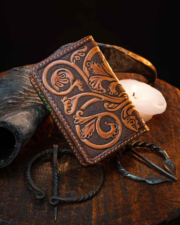 Back view of the handmade leather card holder, showcasing continuous hand-tooled medieval floral scrollwork and a dark textured background.