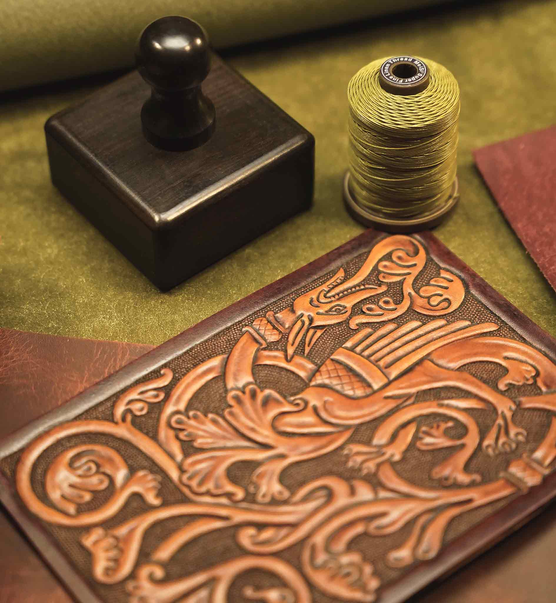 Reliq Leather handmade wallet with medieval dragon tooling in vegetable-tanned leather, shown with linen thread and traditional leatherworking tools.
