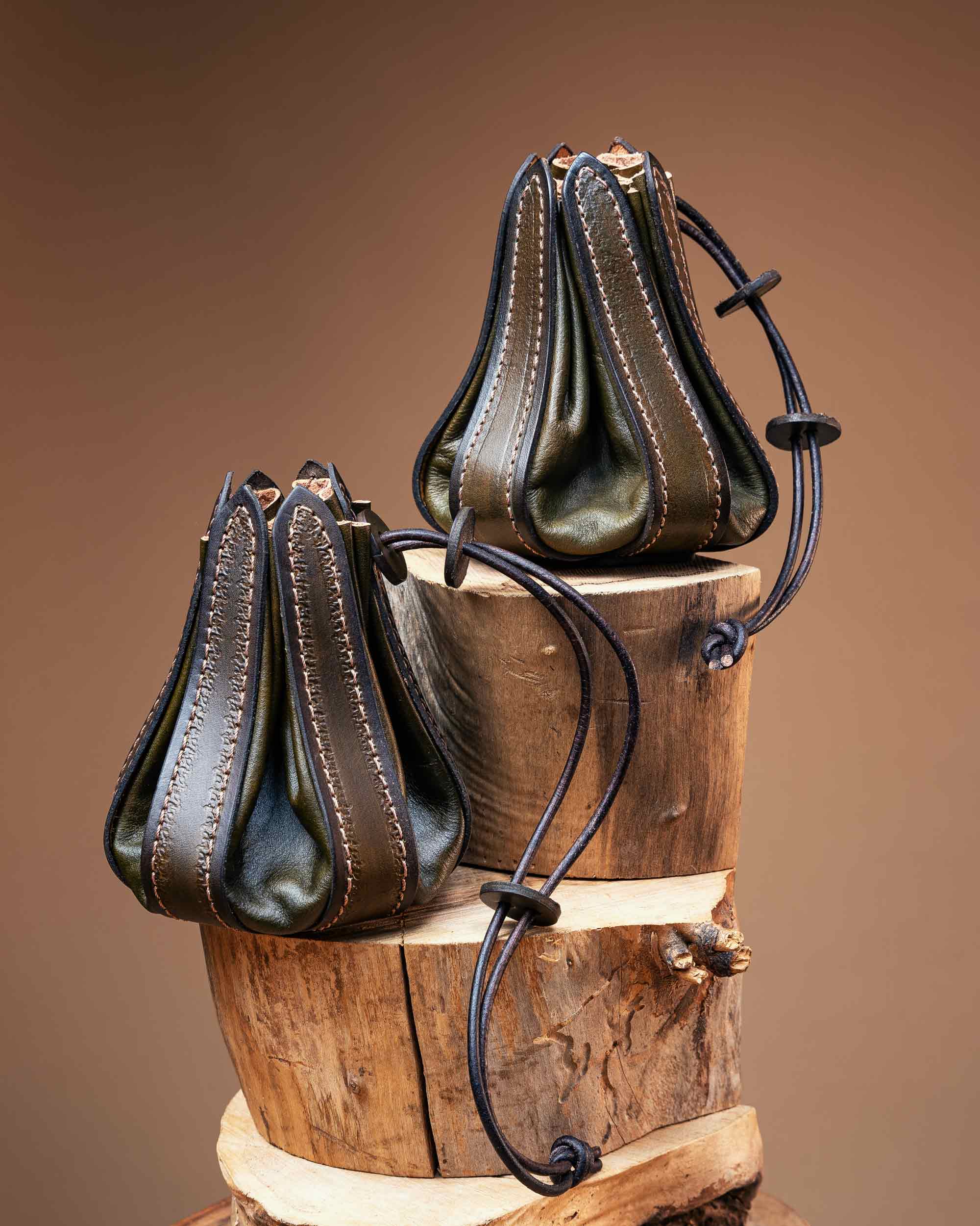 Two olive green artisan leather pouches with a unique gusseted bellows design and sturdy leather drawstrings for tabletop gaming.