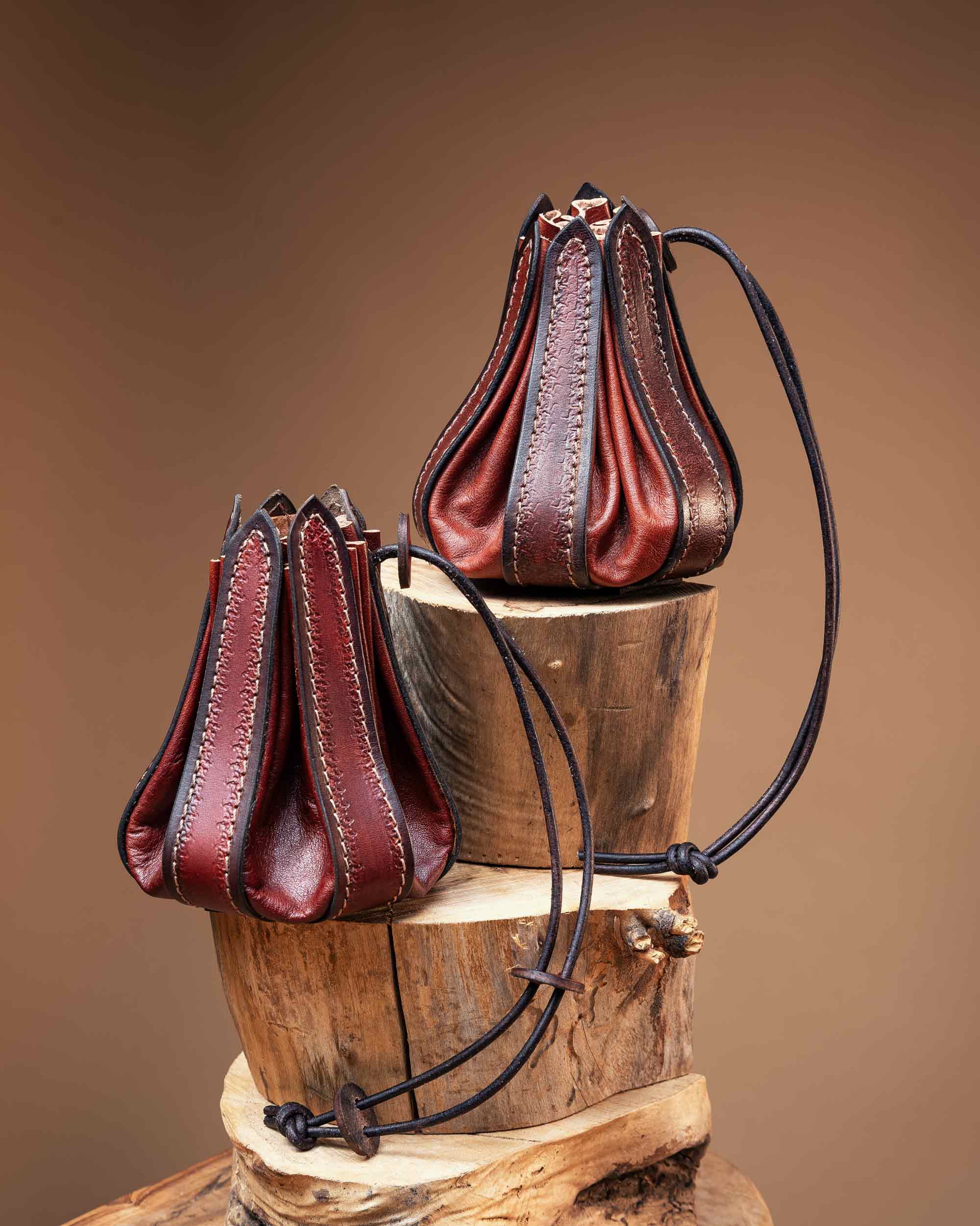 Two rustic red handmade leather bellows pouches, highlighting the intricate edge stitching and functional leather cord closure.