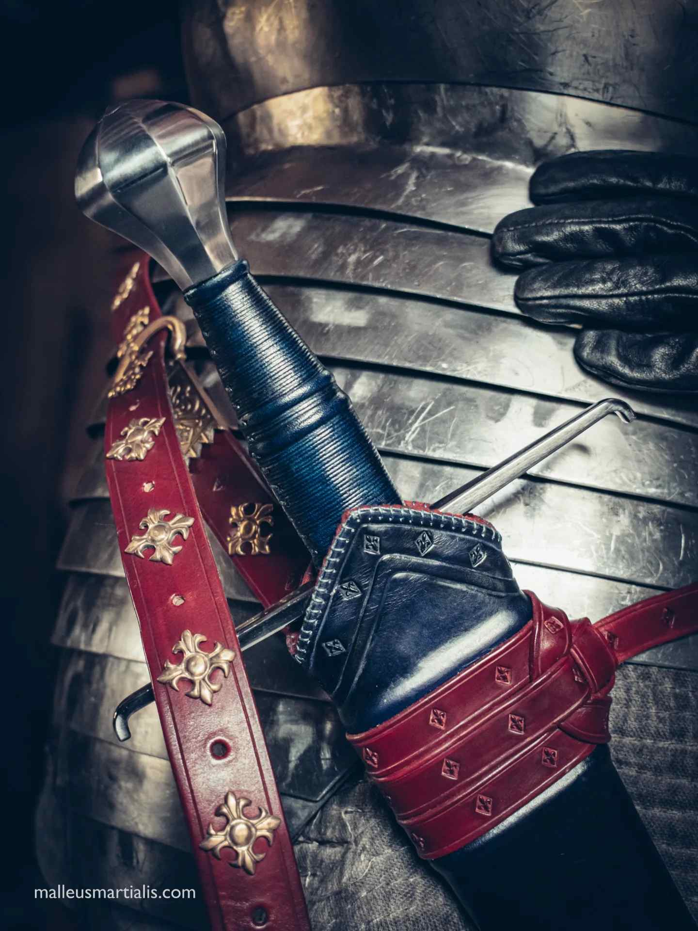 Detailed close-up of a custom handcrafted leather scabbard and red sword belt with brass fittings, commissioned for a Malleus Martialis historical sword, resting against plate armor
