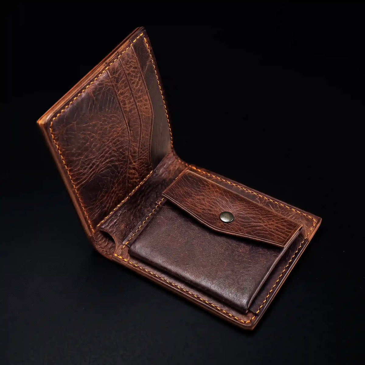 Interior of a dark brown textured leather bifold wallet featuring three curved card slots on the left and a snap-button coin pocket on the right, detailed with orange saddle stitching against a dark background