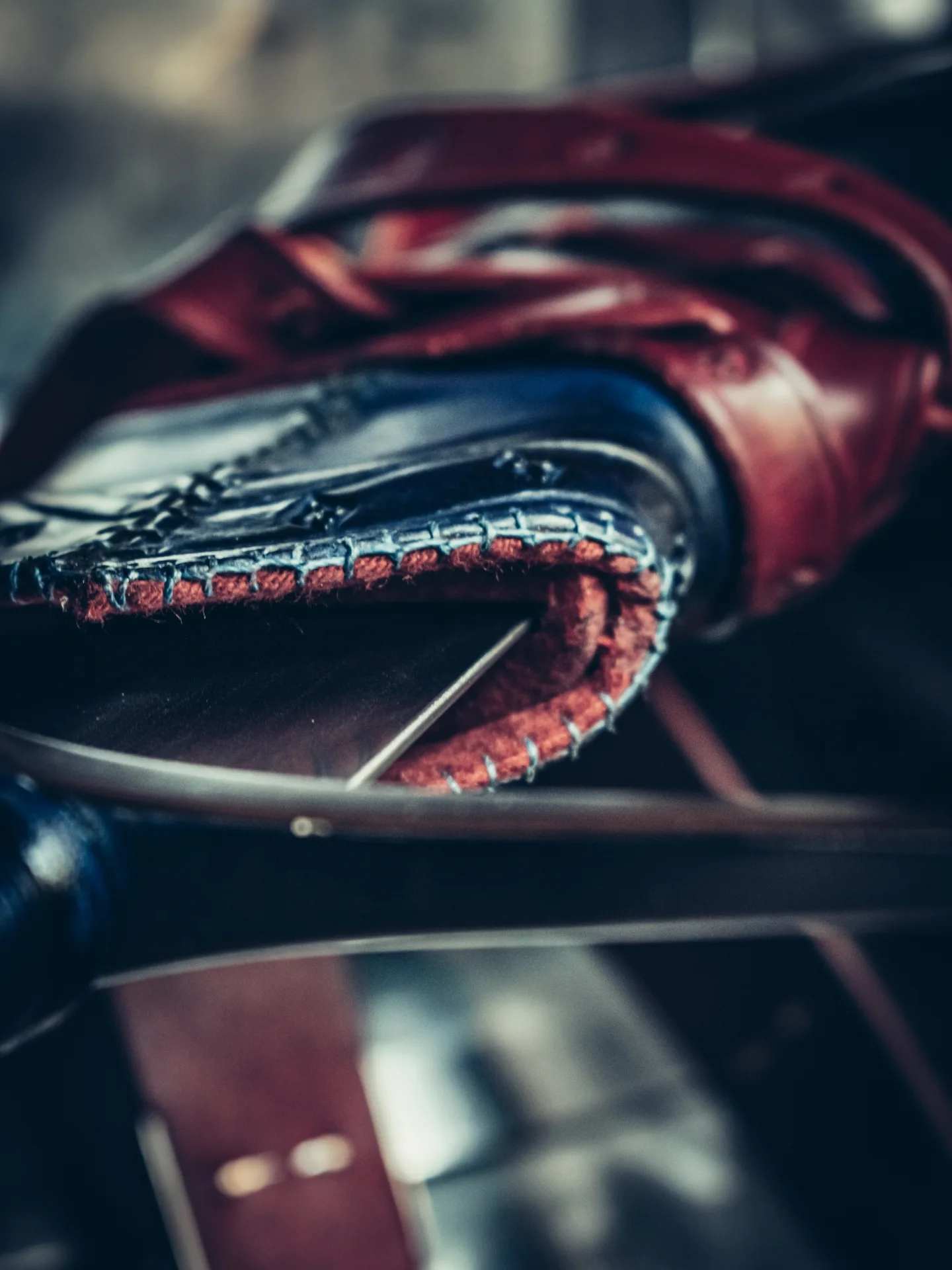 Extreme close-up of the opening of a handcrafted blue leather scabbard, highlighting the meticulous edge stitching, layered construction, and the red interior lining protecting the steel blade