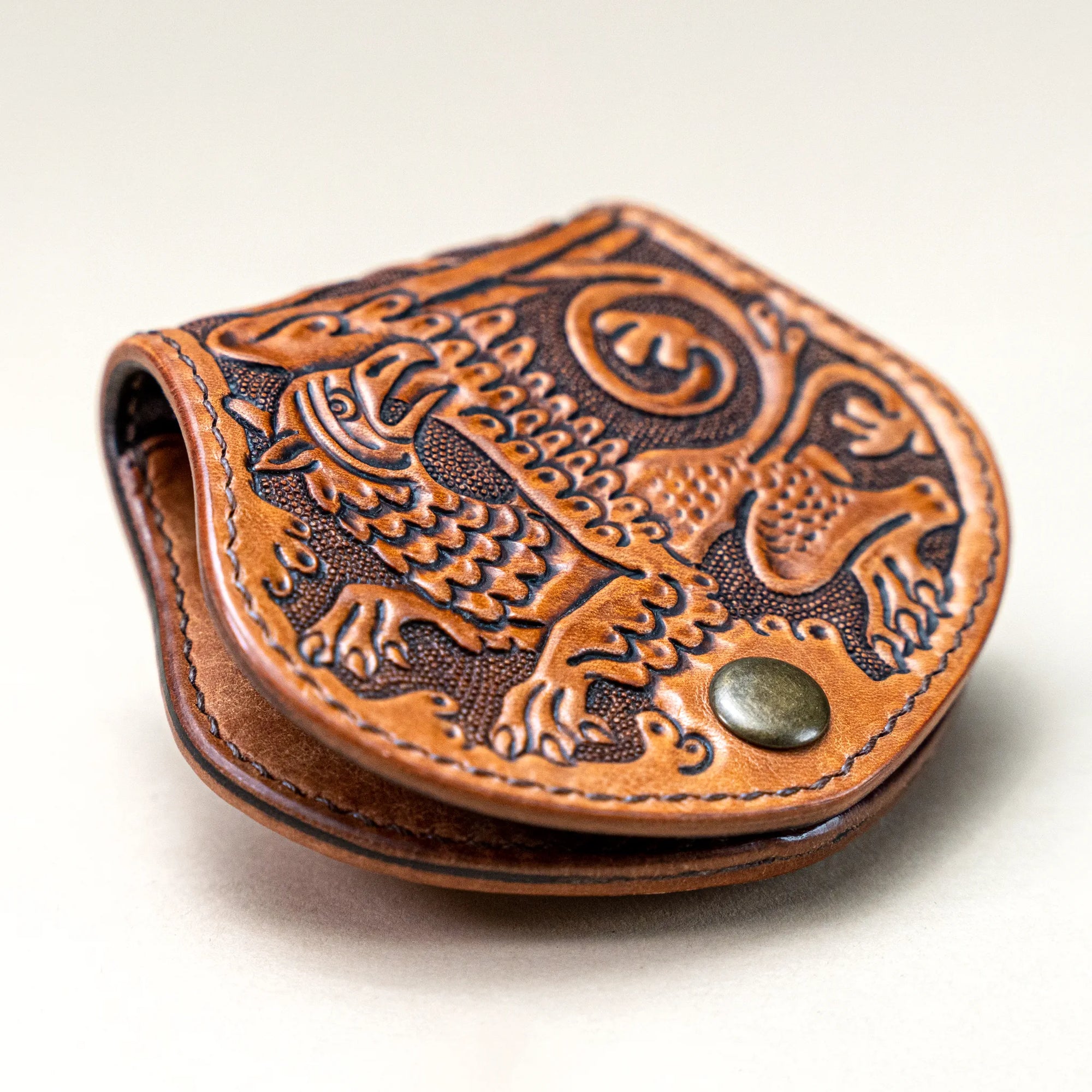 Angled view of Reliq Leather Gryphon handmade coin purse showing compact drop-guard flap and tooling details.