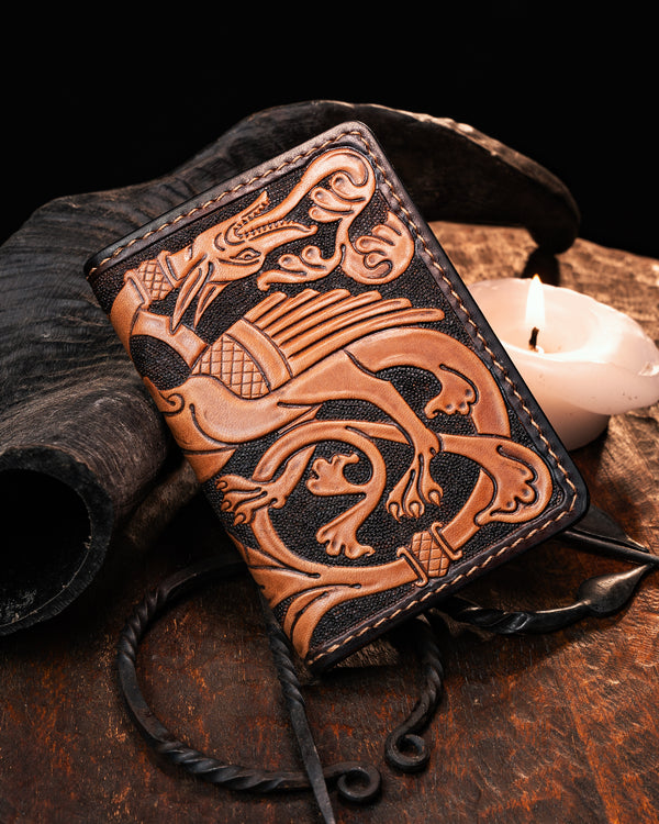 Hand-tooled leather card holder featuring a hand-tooled medieval marginalia dragon. Artisan front pocket wallet inspired by illuminated manuscripts, resting on a rustic wooden surface.