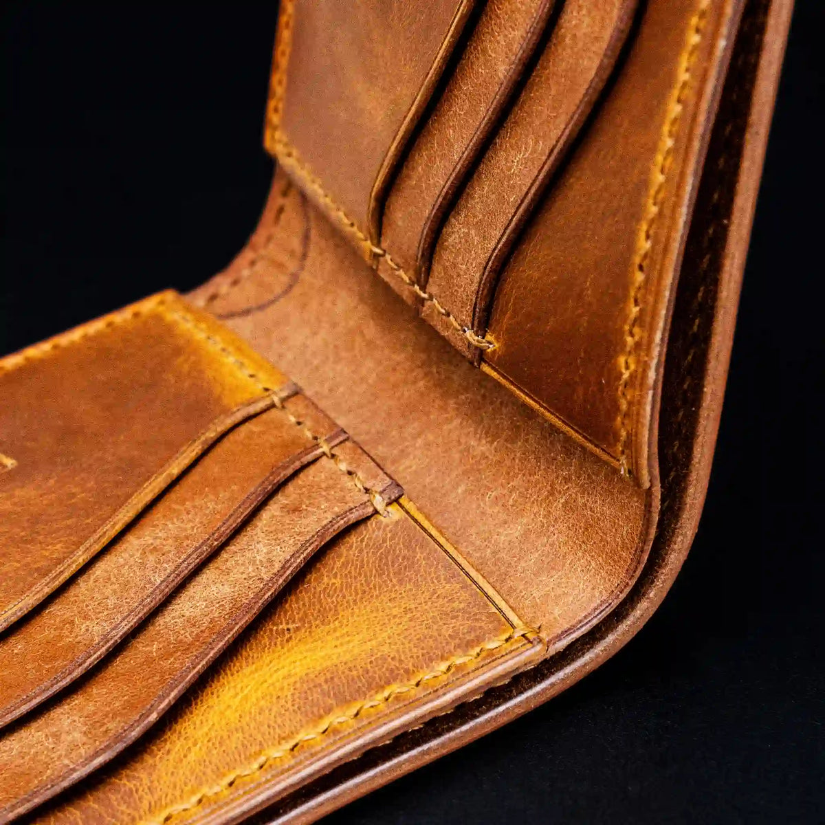 Close-up macro detail of hand-stitched card slots on a vegetable-tanned leather wallet showing natural hide grain texture and edge finishing.